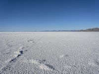 a lone snow field with a mountain in the distance and a person walking on the snow, leaving footprints