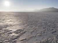 the sun shines brightly over a snow filled expanse with rocks and mountains in the background