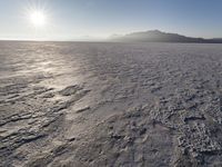 the sun shines brightly over a snow filled expanse with rocks and mountains in the background