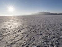 the sun shines brightly over a snow filled expanse with rocks and mountains in the background