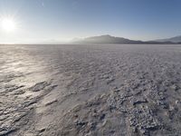 the sun shines brightly over a snow filled expanse with rocks and mountains in the background