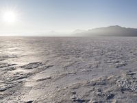 the sun shines brightly over a snow filled expanse with rocks and mountains in the background
