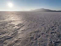 the sun shines brightly over a snow filled expanse with rocks and mountains in the background