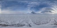 a field covered in snow and white snow with clouds above it as if seen through a fish eye