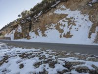 a person riding on the back of a motorcycle down a road covered in snow next to a cliff