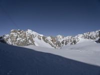 a lone skier is skiing through the snow in front of mountains under a clear blue sky