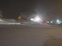 a snow covered park area at night with buildings and trees on the other side of it