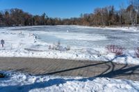 a pond with snow on the ground and a brick path near it and a sign pointing to the water