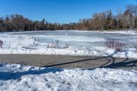 a pond with snow on the ground and a brick path near it and a sign pointing to the water