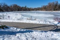 a pond with snow on the ground and a brick path near it and a sign pointing to the water