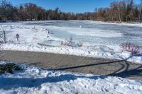 a pond with snow on the ground and a brick path near it and a sign pointing to the water