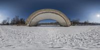 a winter park covered with lots of snow and a large arched archway with a clock