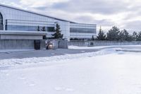 a parking lot covered in snow near a building, and people walking with backpacks