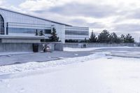 a parking lot covered in snow near a building, and people walking with backpacks