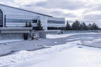 a parking lot covered in snow near a building, and people walking with backpacks