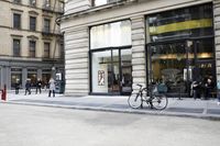 some people are riding bikes down the street by a building or restaurant and other vehicles