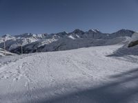 a snowy ski slope on which the skier is going down the hill and into the mountains