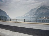 person riding on a bike near an empty road near the water in front of mountains