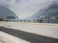 person riding on a bike near an empty road near the water in front of mountains