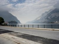 person riding on a bike near an empty road near the water in front of mountains