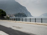 person riding on a bike near an empty road near the water in front of mountains