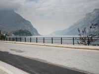 person riding on a bike near an empty road near the water in front of mountains