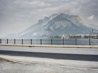 person riding on a bike near an empty road near the water in front of mountains
