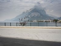 person riding on a bike near an empty road near the water in front of mountains