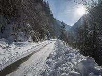 there is snow on the road that goes from the mountains to the trees along with the sun shining through the clouds