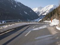 a car travels down the street through the mountains in wintertime near snowy slopes and snow