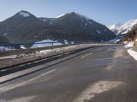 a car travels down the street through the mountains in wintertime near snowy slopes and snow