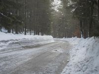 a narrow snow - covered road is next to the pine trees with snow all around it