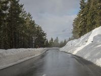 a narrow snow - covered road is next to the pine trees with snow all around it