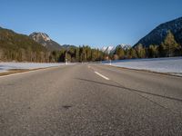 an empty road with snow capped mountains in the background and a car on the side driving on it