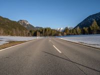 an empty road with snow capped mountains in the background and a car on the side driving on it