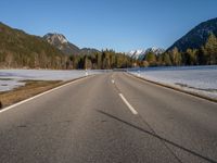 an empty road with snow capped mountains in the background and a car on the side driving on it