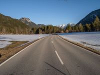 an empty road with snow capped mountains in the background and a car on the side driving on it