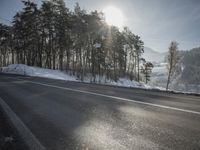 the road has been snow covered, so the sun is setting in the distance below the tree line