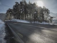 the road has been snow covered, so the sun is setting in the distance below the tree line