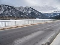 a road in front of snow covered mountains with a fence around it and the snow covered mountain