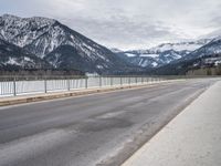 a road in front of snow covered mountains with a fence around it and the snow covered mountain