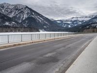 a road in front of snow covered mountains with a fence around it and the snow covered mountain