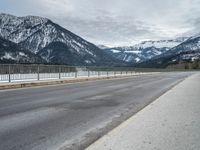 a road in front of snow covered mountains with a fence around it and the snow covered mountain