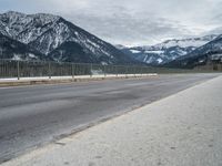 a road in front of snow covered mountains with a fence around it and the snow covered mountain