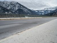 a road in front of snow covered mountains with a fence around it and the snow covered mountain