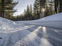 a road is covered in snow near a pine tree filled hill with trees and some snow