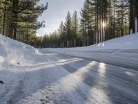 a road is covered in snow near a pine tree filled hill with trees and some snow