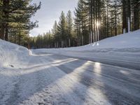 a road is covered in snow near a pine tree filled hill with trees and some snow