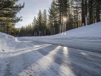 a road is covered in snow near a pine tree filled hill with trees and some snow