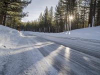 a road is covered in snow near a pine tree filled hill with trees and some snow